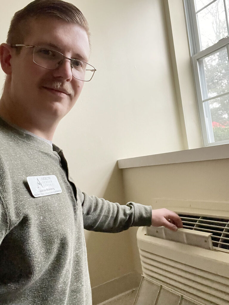 A man in a green shirt stands by an air conditioner, cleaning the AC room filter.
