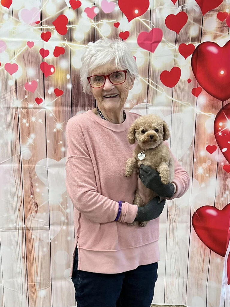 Senior lady cuddling small dog against heart backdrop during Valentine's Day celebration.