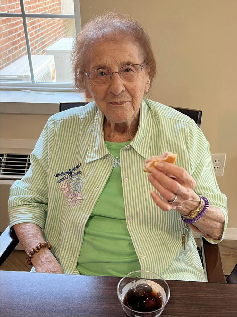 In honor of Asian American, Native Hawaiian, and Pacific Islander Heritage Month, an elderly woman sits at a table with a sandwich and an iced drink for Hawaii Happy Hour.