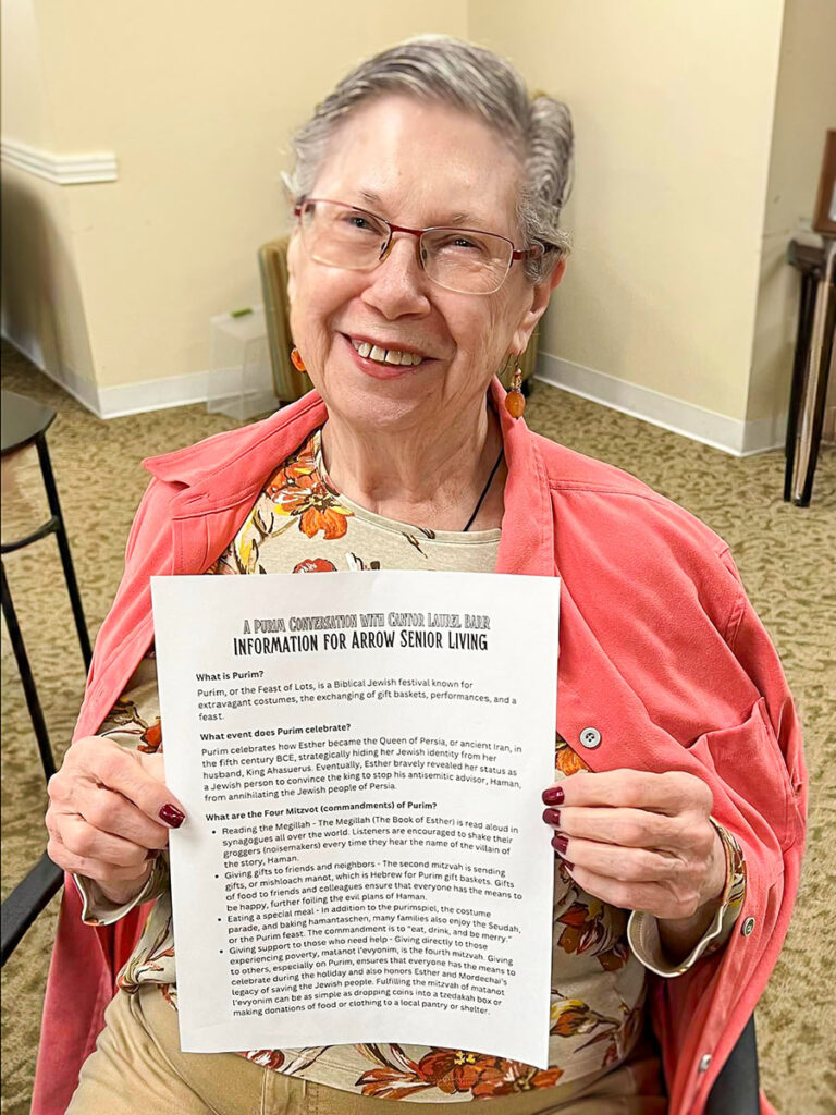 A lady sitting down with a pink jean jacket proudly displays an information flyer. She is the Senior Resident Ambassador at the D&I Purim Conversation.