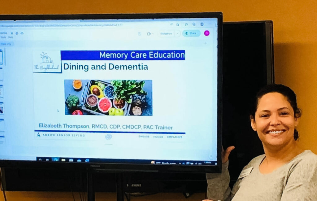 Memory Care Education session on 'Dining and Dementia,' with a presenter smiling beside the screen displaying food options for dementia care.