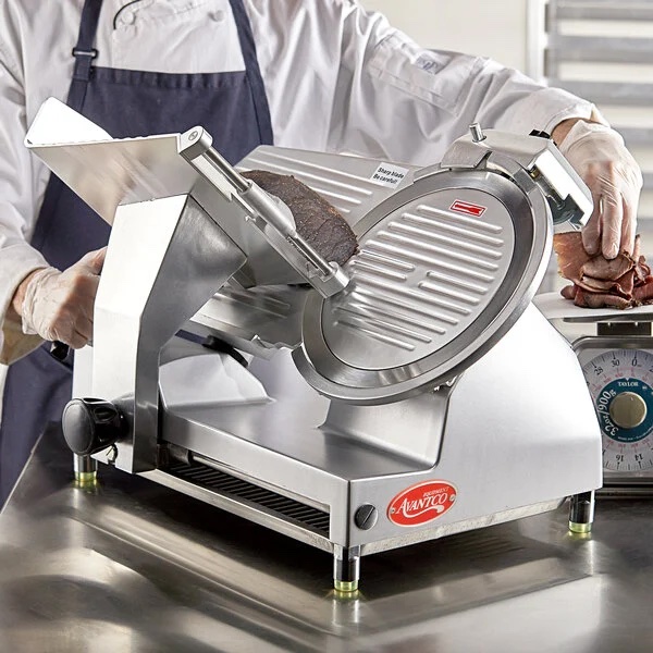 Chef using a commercial Avantco meat slicer to cut thin slices of roast beef in a professional kitchen setting, wearing gloves and apron.