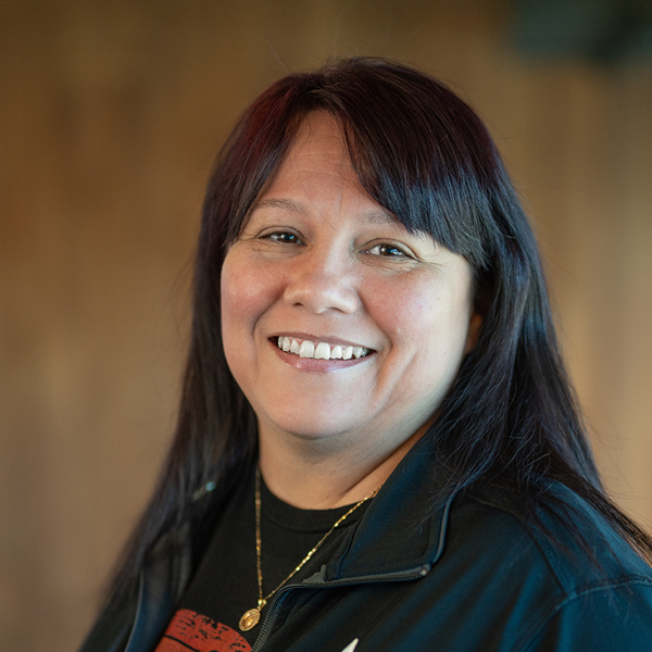 Robin Benavides, Memory Care Director at Carriage Court Senior Living, smiles in a warmly lit indoor headshot, wearing a black jacket with long dark hair.