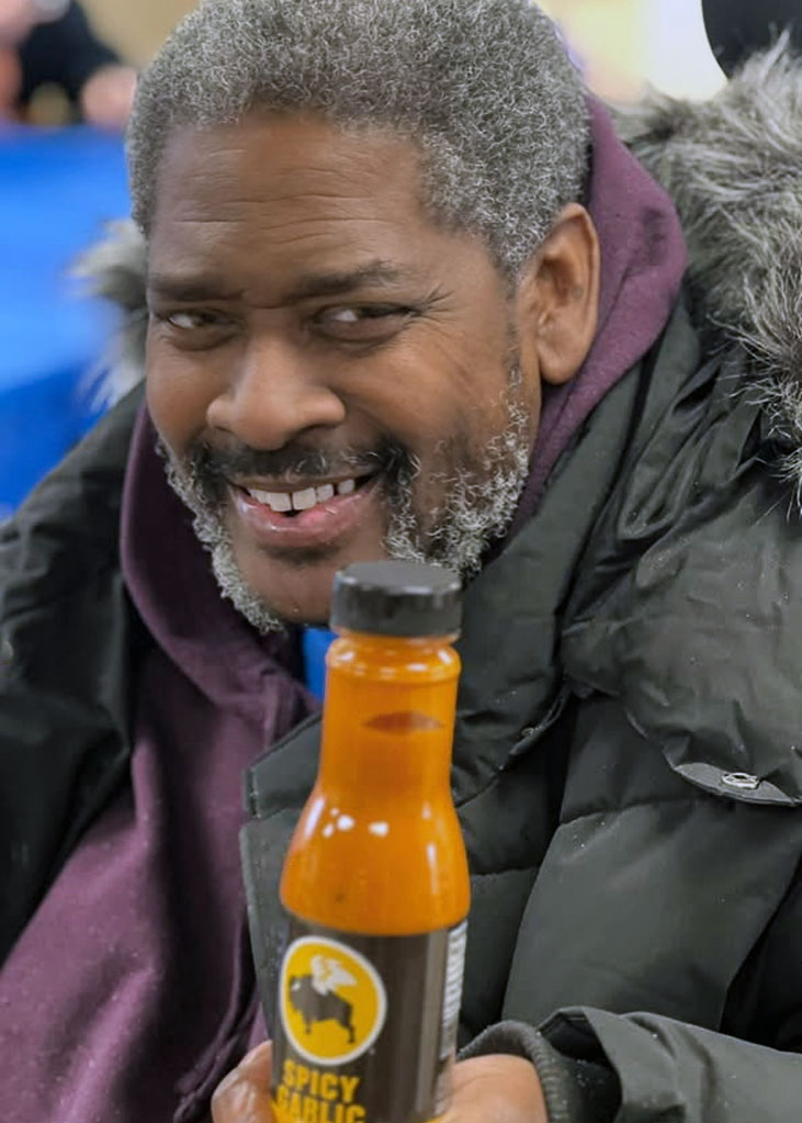A resident at Carriage Court smiles brightly, holding a bottle of spicy sauce.