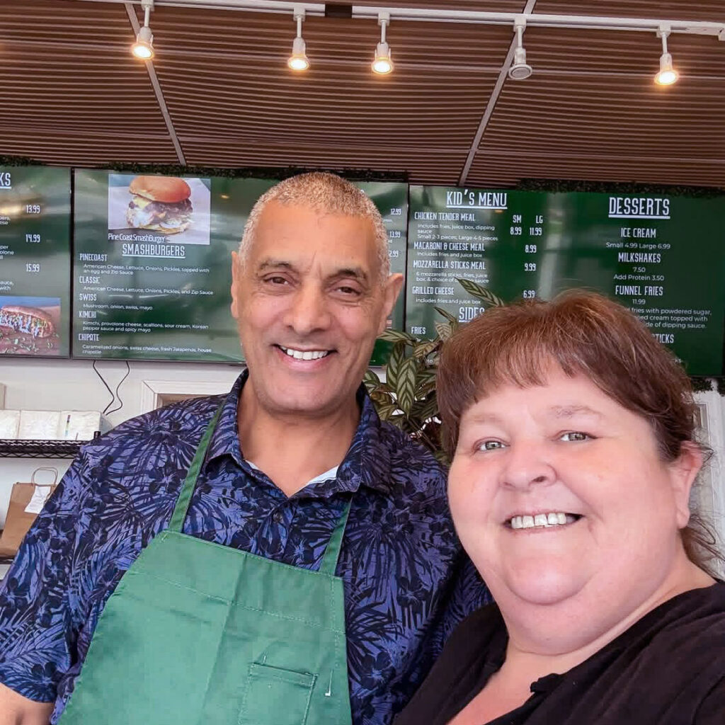 A Carriage Court team member smiles alongside a local business owner wearing a green apron.