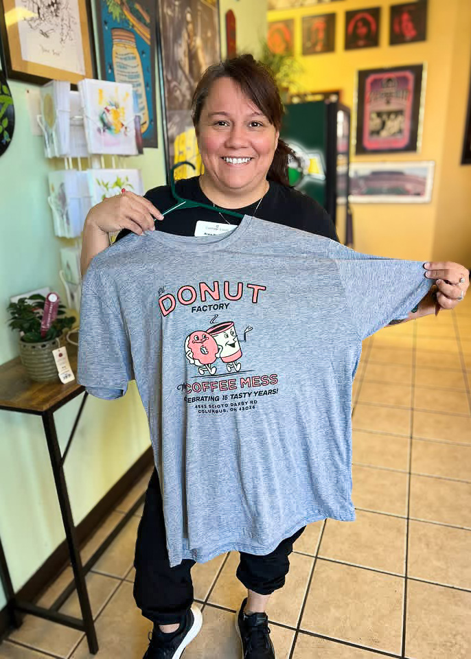 A woman smiles, holding up a t-shirt.