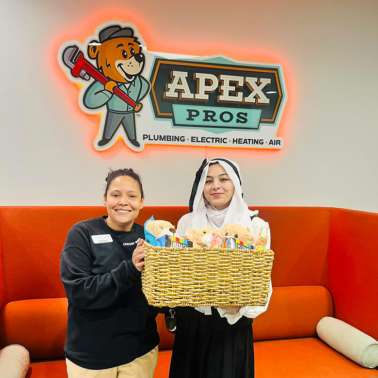 A team member at Carriage Court presents a very large gift basket to a smiling business owner at Apex Pros.