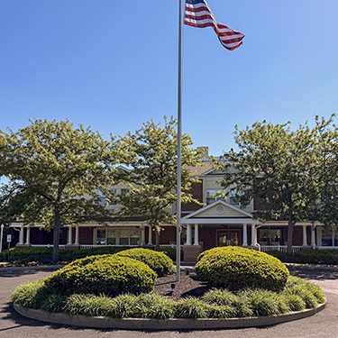 The exterior of Carriage Court Senior Living, showcasing landscaping and flag.