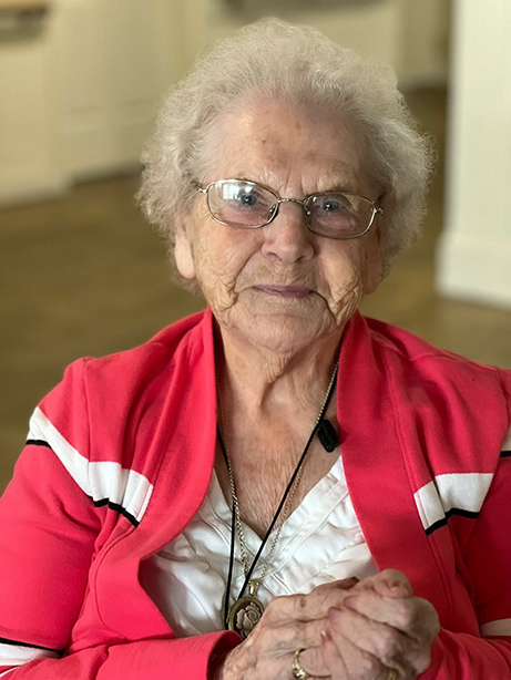 A senior woman wearing a red striped jacket smiles at Carriage Court Senior Living.